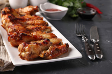 Grilled chicken wings on a white plate and tomato sauce on dark background