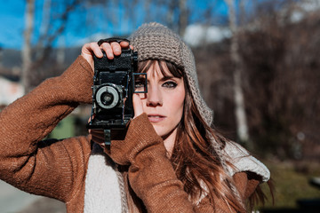 Portrait of a young photographer dressed in brown winter clothes, using an old photographic camera.