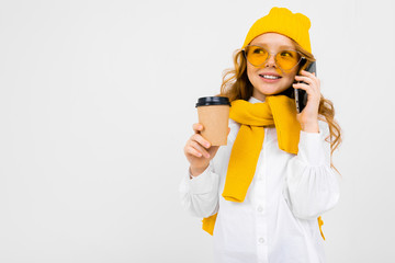 girl in a winter hat and scarf with a glass of hot drink and a smartphone in her hands on a white background with copy space