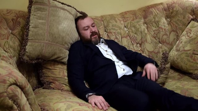 A tired man in a suit falls on the sofa after a hard day's work.