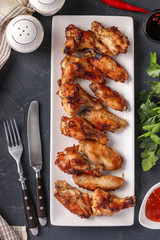 Grilled chicken wings on a white plate and tomato sauce on dark background, Top view