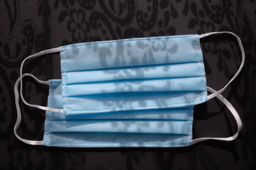 Two light blue medical disposable face masks on the dark black background with shadows ornaments againts virus covid-2019. Heath care concept, quarantine, stop coronavirus