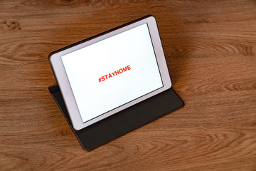 Stay Home inscription on tablet, mobile phone. Stay at home advice to stop coronavirus COVID-19 spreading. On wooden background. Concept how to stop the coronavirus from spreading