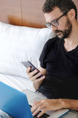 Young man is working from home during Coronavirus or Covid-19 quarantine. Man laying on bed using laptop and phone for his work during self isolation