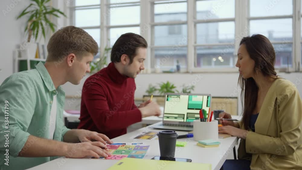Wall mural zoom out and in shot of team of three marketing specialists and designers sitting at desk in office 