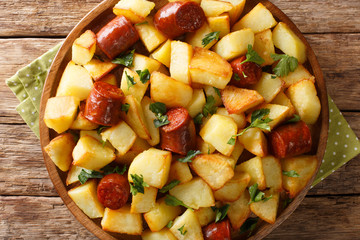 Tasty crispy fried potatoes with sausages and herbs close-up in a plate. Horizontal top view