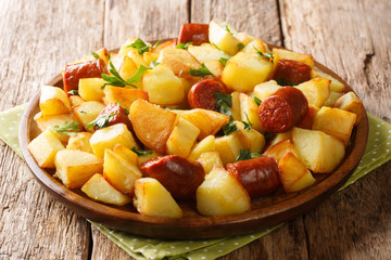 Fried potato recipe with spicy sausages and fresh parsley close-up in a plate. horizontal
