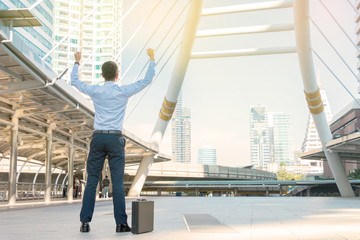 Successful businessman celebrating his victory with arms up  on cityscape background.