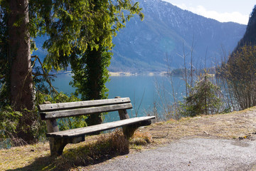 Empty wooden bench on shore of beuatiful lake in austrian Alps. Winter sunny morning on lake Hallstatt. The most beautiful lake to explore in Austria.