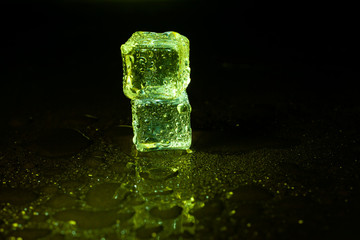 Green ice cubes on black table background.