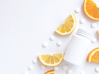 scattered vitamin pills and bottle with lemon orange on white background. Copyspace, flat lay, close up. Concept boost immune system, medicine and tablets.