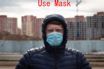 A young man in a medical mask on a stain background of houses under construction