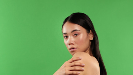 Fototapeta premium Beautiful woman portrait, beauty on green background, Asian woman standing half-turned holding her shoulder and looking at camera