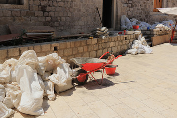 A construction site under construction in the middle old town Dubrovnik. Building new path. Worker repair damaged parts of wall and castle. Bags with sand, bricks, tools for job, bucket. Croatia