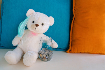 Teddy bear with surgical face mask holding glass bottle money savings with coins in hand worry about illness, insufficient money to pay medical expenses. Health insurance, medicare and finance concept
