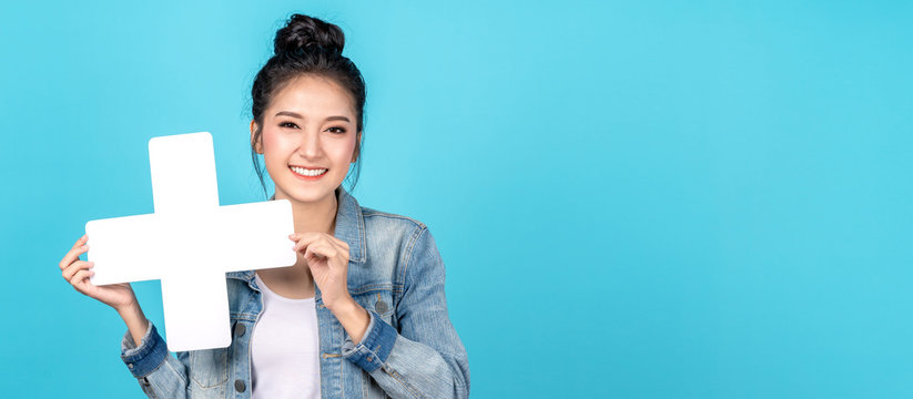 Banner of Happy asian woman smiling and holding plus or add sign on copy space blue background. Cute asia girl smiling wearing casual jeans shirt and showing join sign for increse and more concept