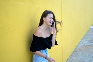 Beautiful girl leaning on yellow wall, young friendly woman smiling happy on a sunny day of summer