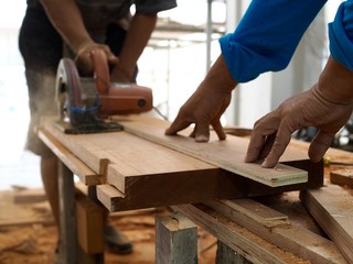 The hand of a man was helping to hold the wood to not move ,the carpenter to cut wood to make furniture.