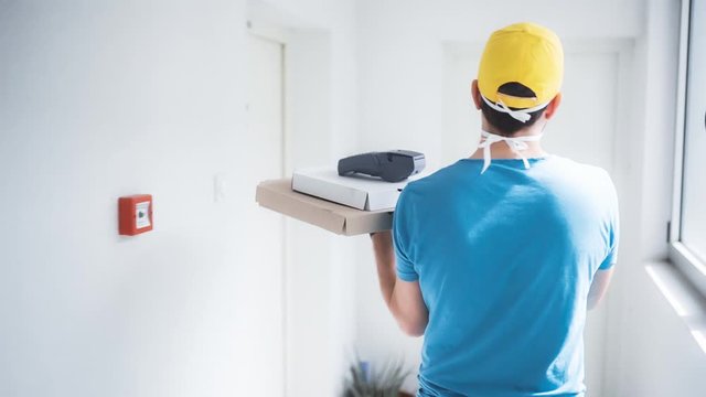 Deliveryman with protective medical mask holding pizza box and POS wireless terminal for card paying - days of viruses and pandemic, food delivery to your home and safety hygiene measures.