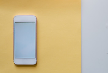 White blank smartphone on pastel yellow background with flower tulips. Minimalistism background. Mock up screen smartphone. Summer or travel concept. Copy space