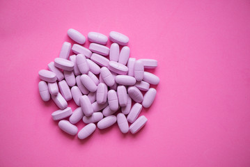 Group of pink pills (tablests) over pink background, top view