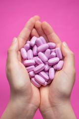 Hands holding plenty of pink pills (tablets) over pink background