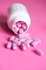 Pink pills out of the plastic bottle, on pink background, selective focus