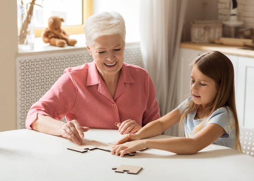 Elderly woman and her grandchild playing puzzle game together in kitchen