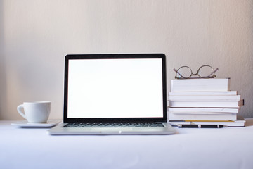  Laptop computer with blank screen in office on the white background with white cup and books. Mock up screen in notebook. White office concept. Minimalism concept