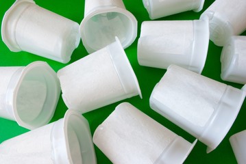 Heap of white yogurt cups scattered on a green background. Ecological concept.
