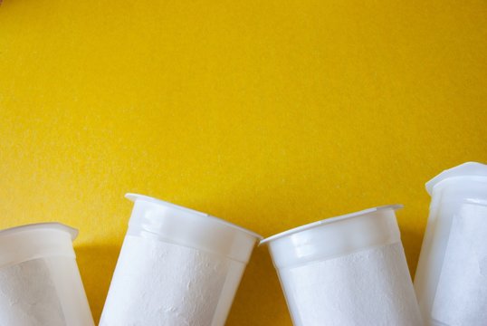 Yellow background with several yogurt cups at the bottom. Ecological concept. Copyspace.