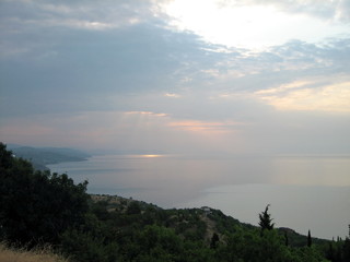 Naklejka premium Sunset through clouds over the sea. The grey sky merges with its reflection in the endless mirror of the sea.