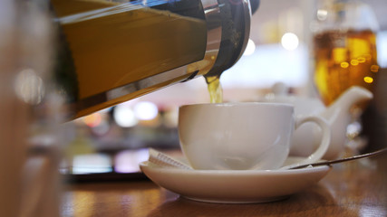 Pouring hot tea into the beautiful english tea cup in breakfast cafe.