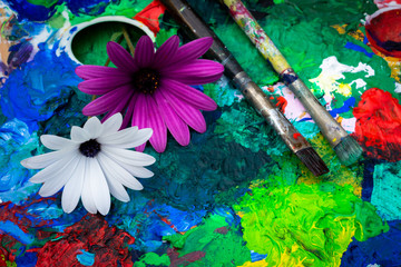 la palette et les pinceaux d'un peintre avec des couleurs et deux fleurs violettes