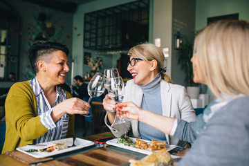 women having lunch together in restaurant, making a toast with wine