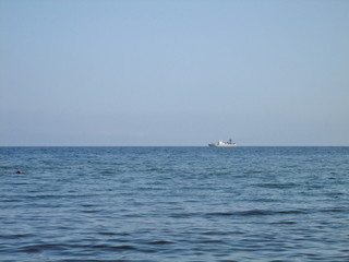 A ship on the roadstead on the horizon between the sky and the sea.