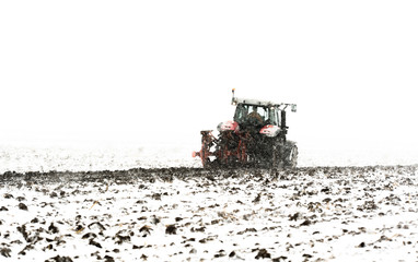 Fototapeta premium Tractor plowing a field in the snow