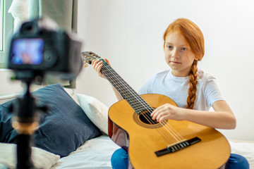 little caucasian blogger girl play guitar at camera. she performs music. enthusiastic self-taught girl with red hair enjoy being interesting for subscribers in her own channel. blog, vlog, music