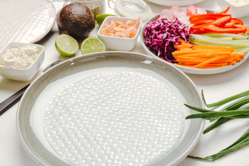 Side view of ingredients for cooking spring rolls with avocado and shrimps, rice paper and soy sauce on a white background.
