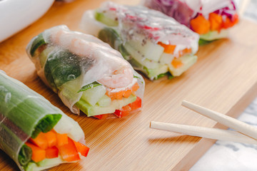 Close up of fresh spring rolls with shrimp and vegetables and different sauces served on a wood plate with chop sticks.