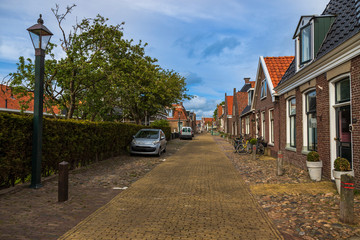 Street with houses and cars in Hindeloopen in the Netherlands. The background is a blue sky with clouds.