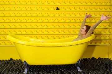Frau im Abendkleid freut sich in gelber Badewanne