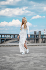 Charming long-haired blonde in a white tight-fitting dress walks around the city