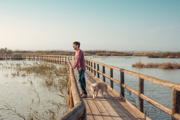 Man and dog looking to the horizon in a natural environment of lagoon and pier - Weekend sunset with puppy