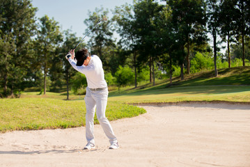 Asian man golfer hitting ball on sand at golf course
