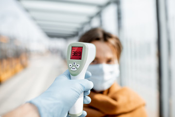 Measuring temperature with infrared thermometer of a young woman in face mask at a checkpoint...