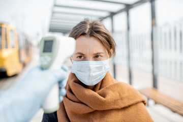 Measuring temperature with infrared thermometer of a young woman in face mask at a checkpoint...