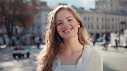 Close up portrait of attractive young woman with frizzy red hair in city center smiling and looking at camera enjoying urban city having fun sun is shining