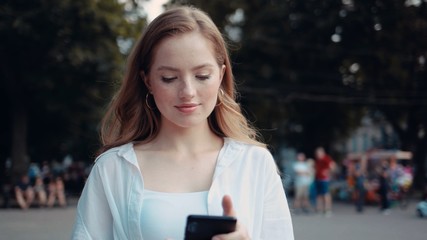 Smiling curly woman walks down the central city street and uses her phone attractive beauty cellphone city device fashion female happy holding lady message mobile outdoor outside