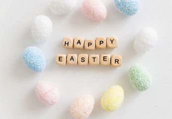 The words Happy Easter made with wooden cubes with letters together with colorful eggs on a white background
